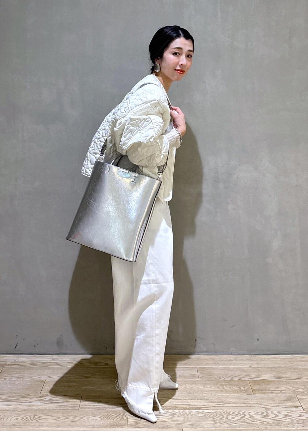 ホワイト系のパンプス、シルバー系のトートバッグ、ホワイト系のデニムパンツを着用したレディースの冬コーディネートの2枚目の写真