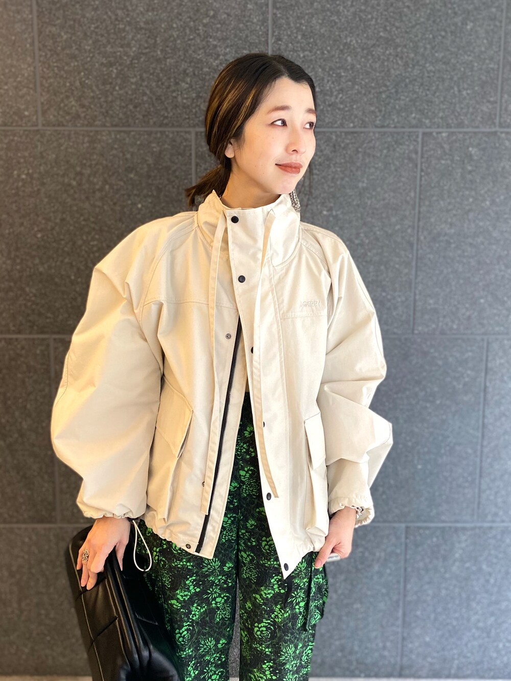 ブラック系のカーゴパンツ、ブラック系のクラッチバッグ、ホワイト系のブルゾンを着用したレディースの春コーディネートの2枚目の写真