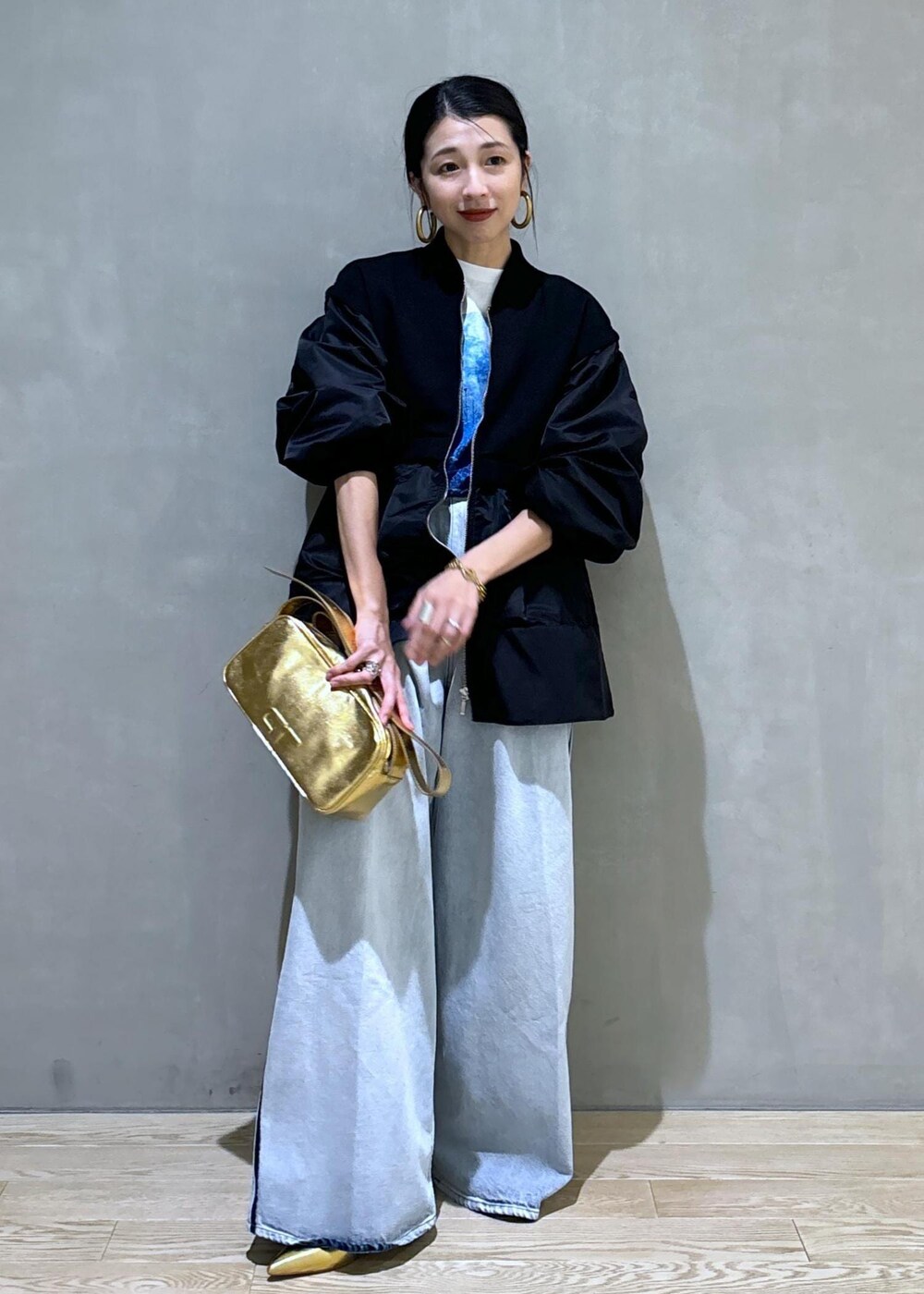 ゴールド系のショルダーバッグ、ブラック系のブルゾン、ホワイト系のTシャツ/カットソーを着用したレディースの秋コーディネートの2枚目の写真