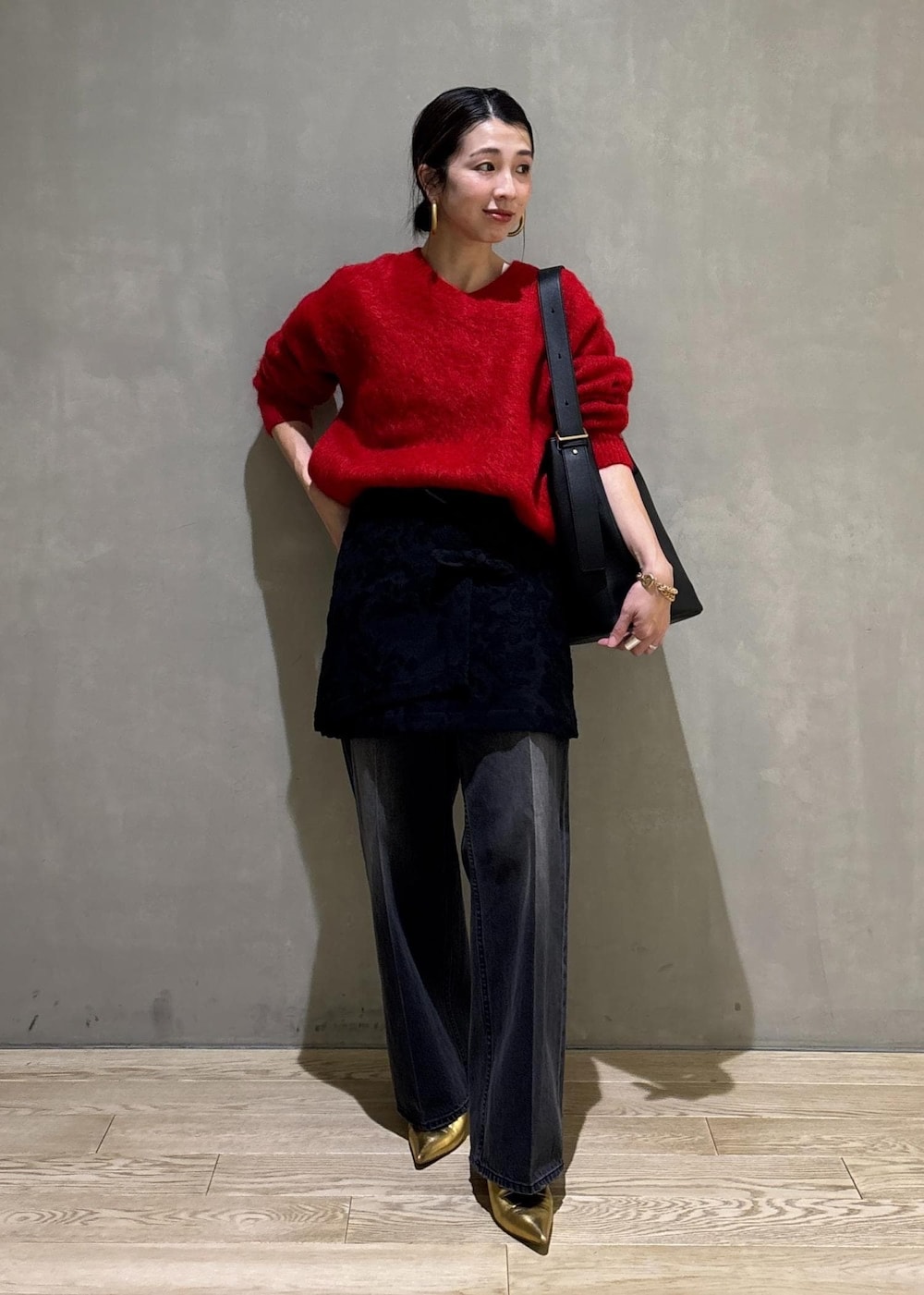レッド系のニット/セーター、ブラック系のスカート、ブラック系のデニムパンツを着用したレディースの冬コーディネートの2枚目の写真