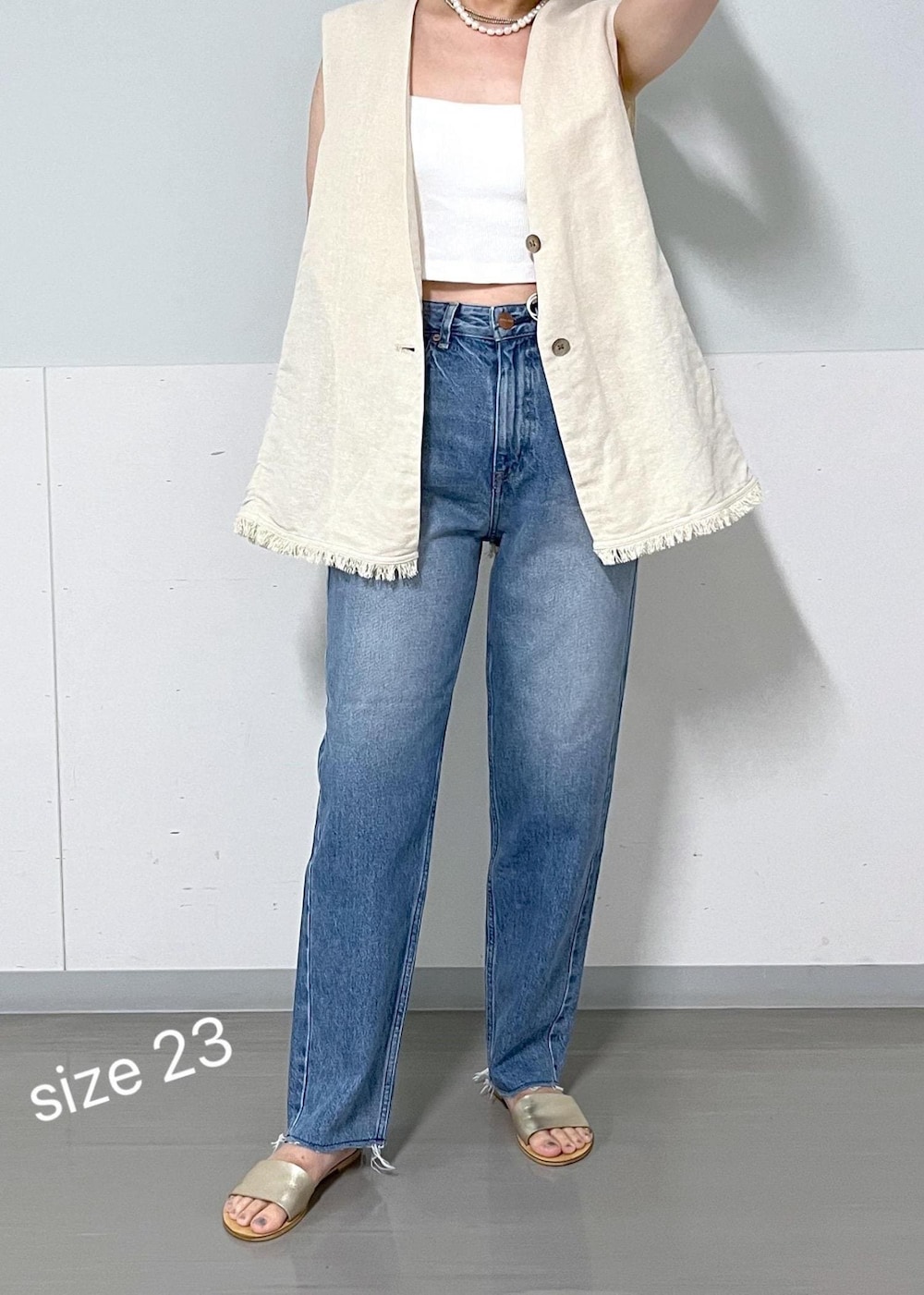 ベージュ系のベスト、ブルー系のデニムパンツを着用したレディースの夏コーディネートの3枚目の写真