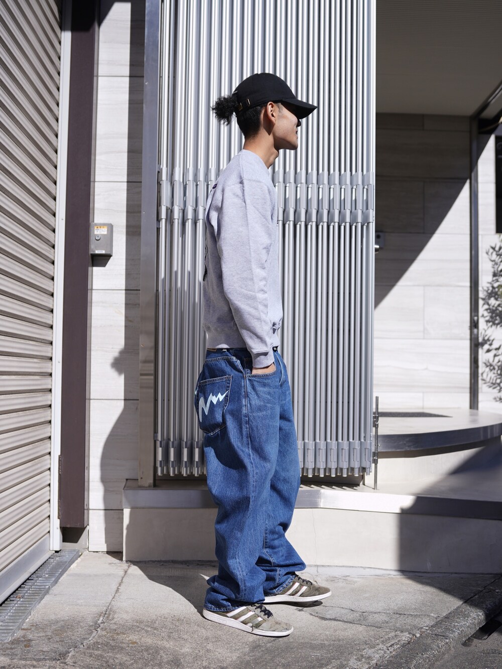 グレー系のスウェット、ブルー系のデニムパンツ、ブラック系のキャップを着用したメンズの冬コーディネートの2枚目の写真