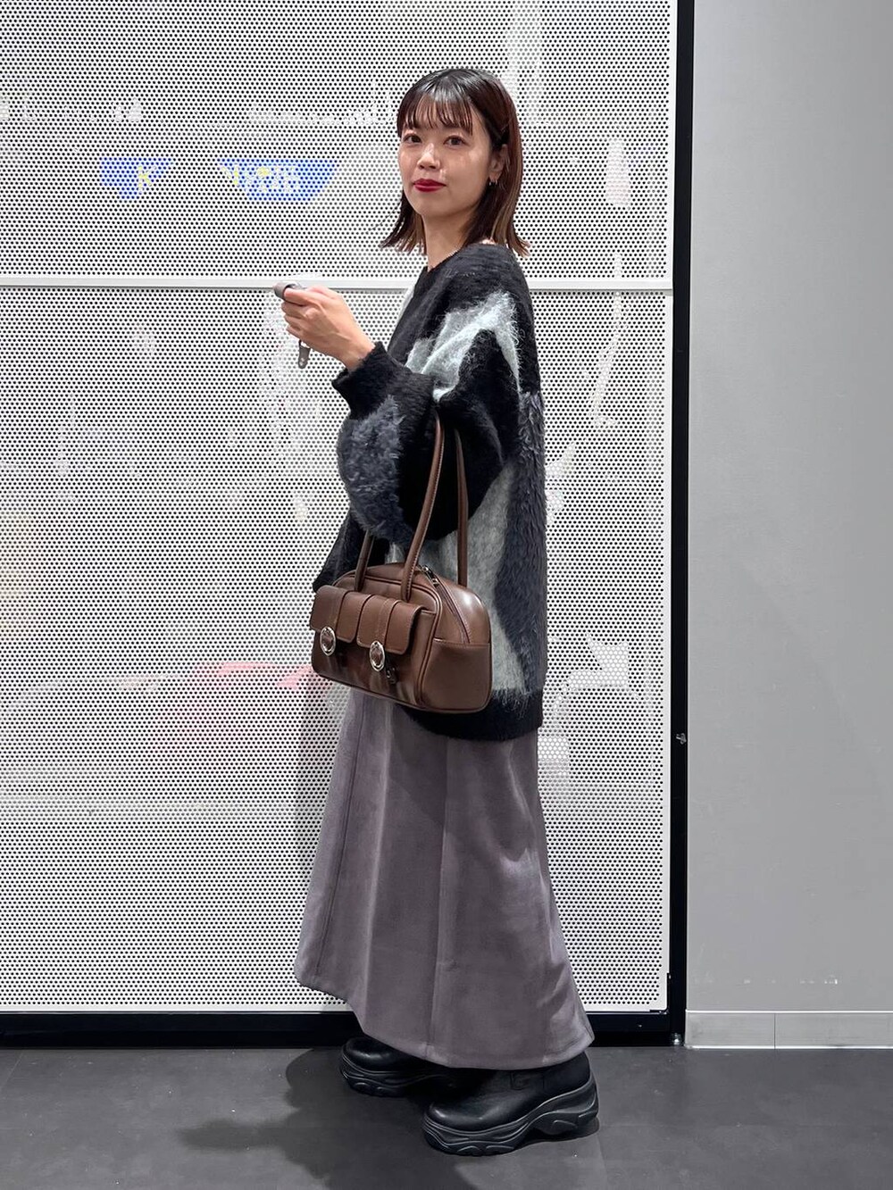 ブラウン系のショルダーバッグ、ブラック系のブーツ、グレー系のスカートを着用したレディースの秋コーディネートの3枚目の写真