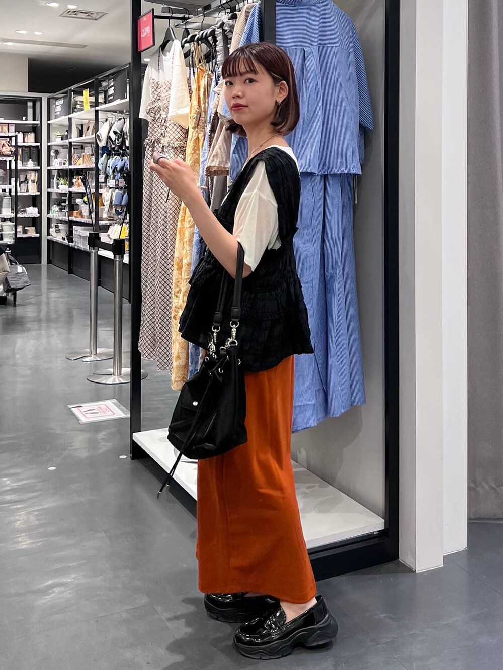 ホワイト系のTシャツ/カットソー、オレンジ系のスカート、ブラック系のローファーを着用したレディースの夏コーディネートの5枚目の写真