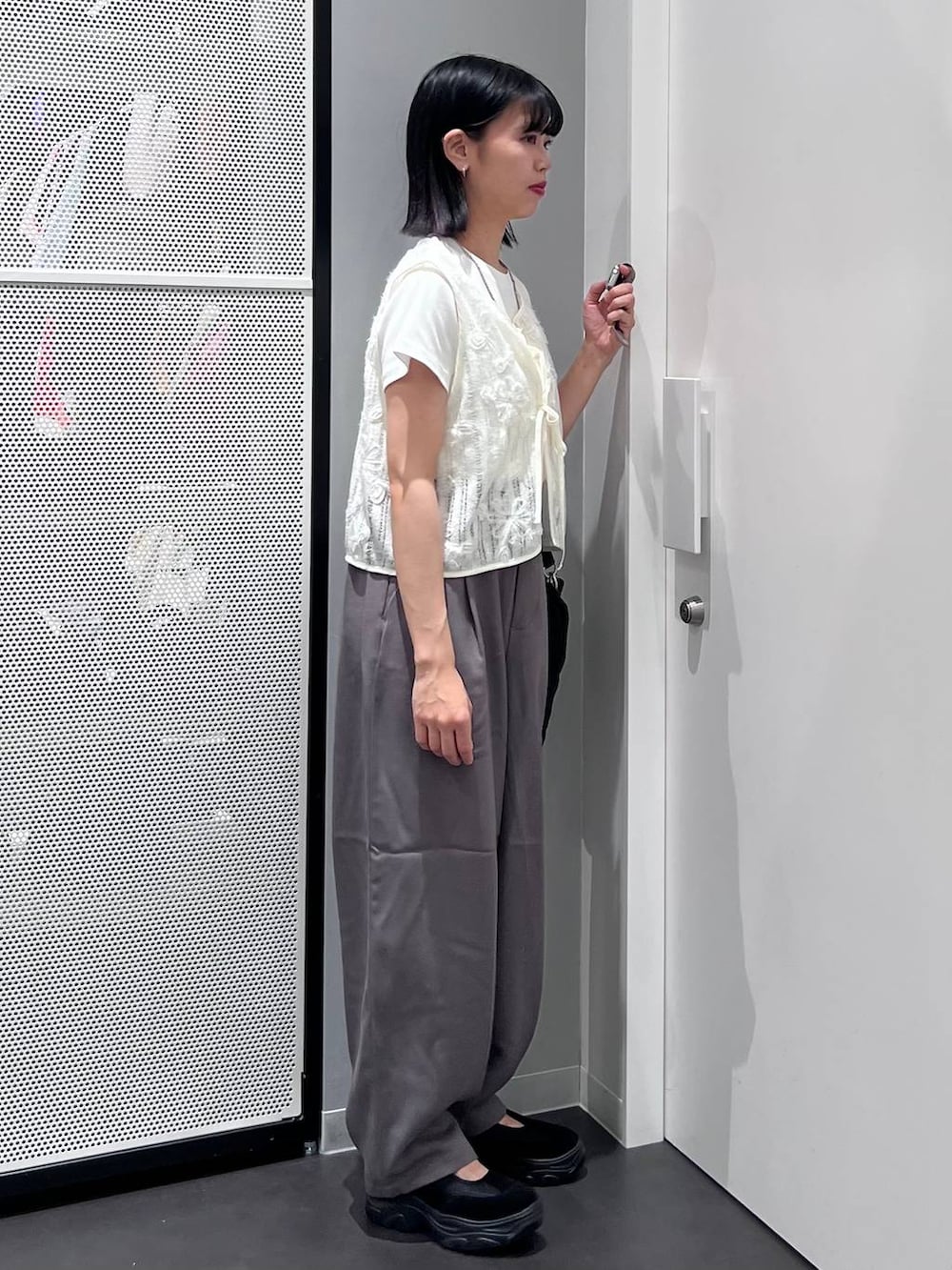ブラック系のハンドバッグ、グレー系のスラックス、ホワイト系のTシャツ/カットソーを着用したレディースの夏コーディネートの2枚目の写真