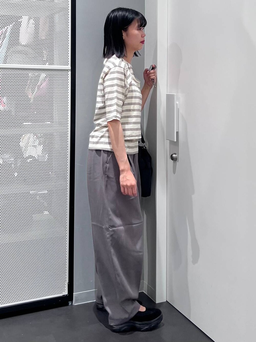 ブラック系のハンドバッグ、グレー系のスラックス、ベージュ系のTシャツ/カットソーを着用したレディースの夏コーディネートの3枚目の写真
