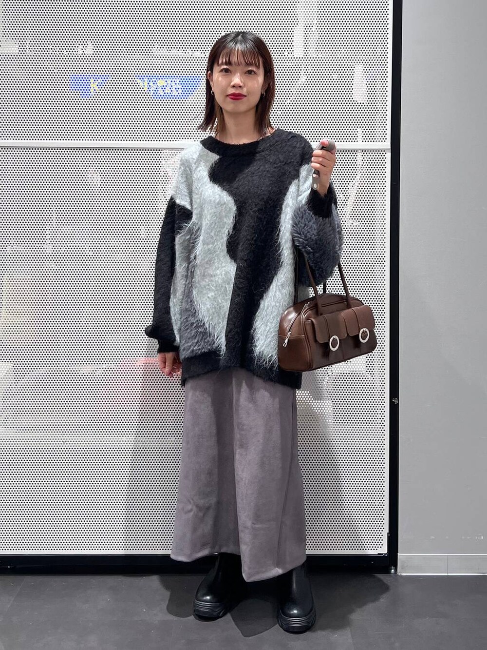 ブラウン系のショルダーバッグ、ブラック系のブーツ、グレー系のスカートを着用したレディースの秋コーディネートの2枚目の写真