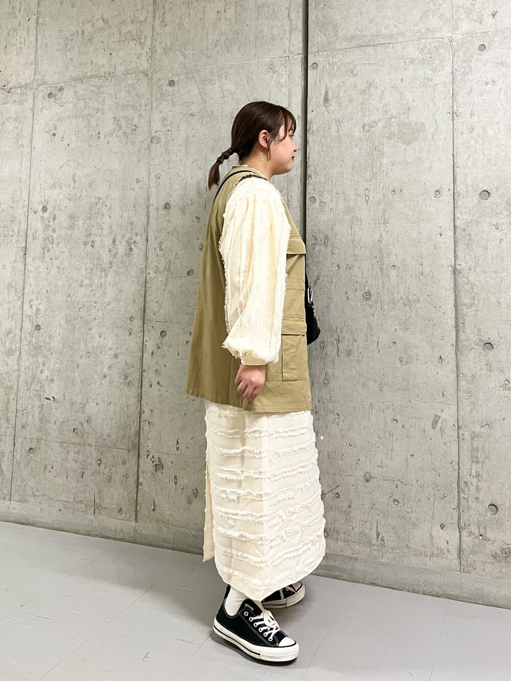 ベージュ系のベスト、ブラック系のショルダーバッグ、ホワイト系のワンピースを着用したレディースの春コーディネートの2枚目の写真