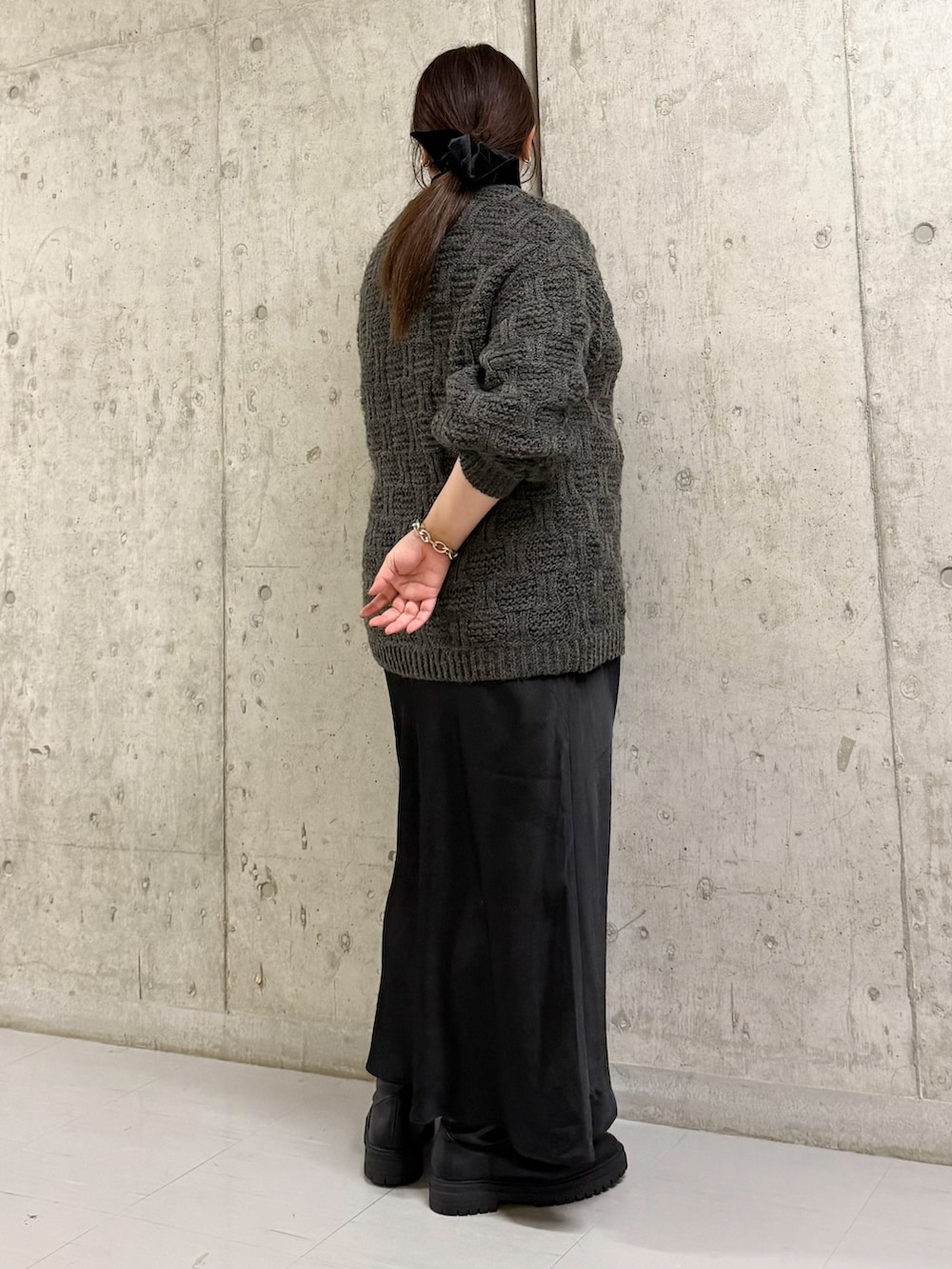 グレー系のニット/セーター、ブラック系のスカート、ブラック系のブーツを着用したレディースの冬コーディネートの2枚目の写真