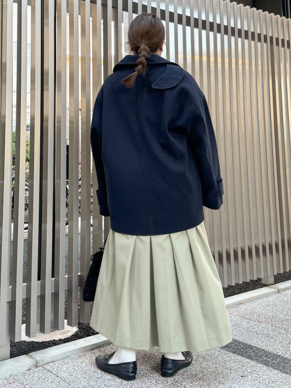 ブルー系のステンカラーコート、グリーン系のワンピース、ブラック系のショルダーバッグを着用したレディースの秋コーディネートの3枚目の写真