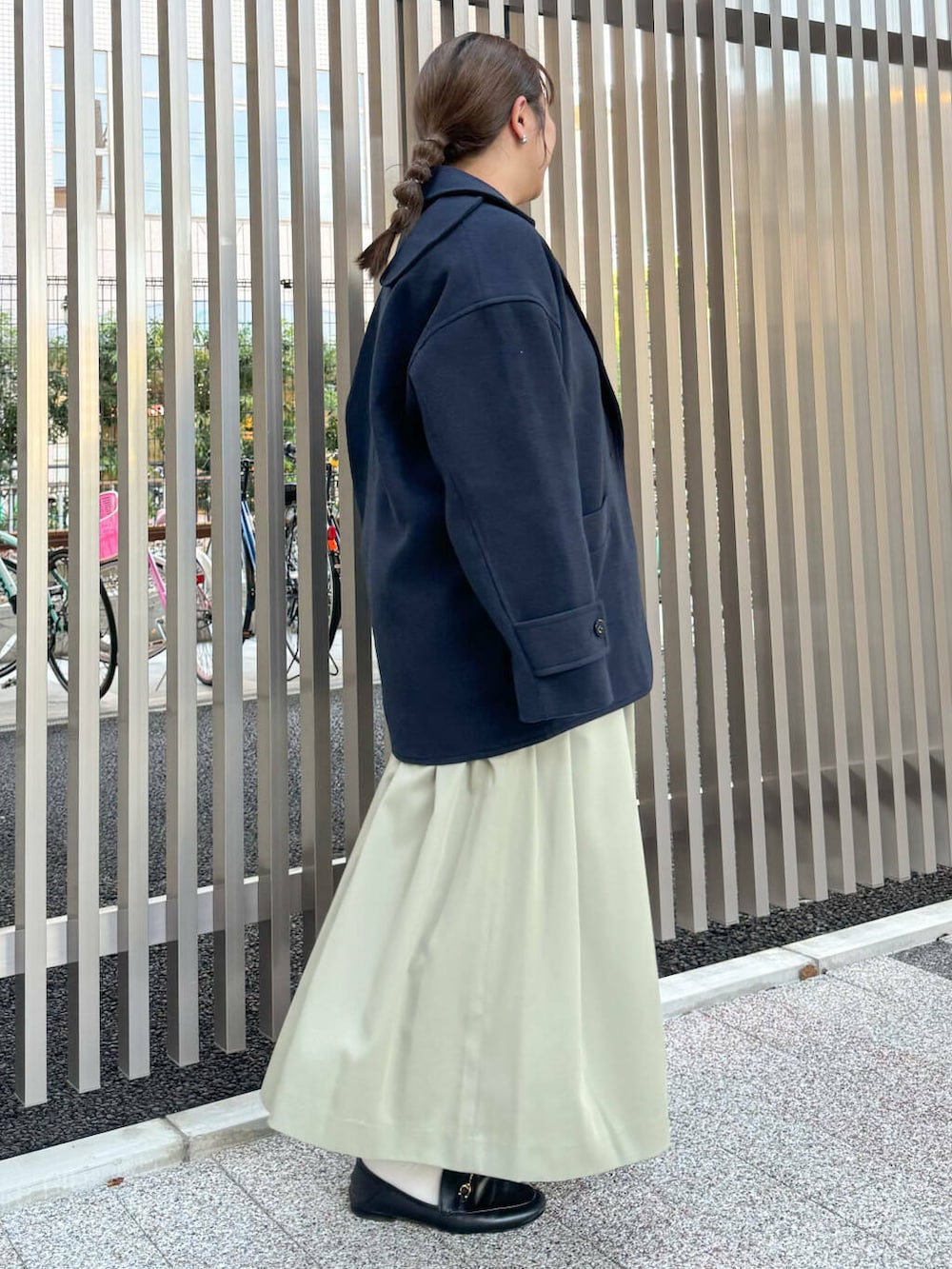 ブルー系のステンカラーコート、グリーン系のワンピース、ブラック系のショルダーバッグを着用したレディースの秋コーディネートの2枚目の写真