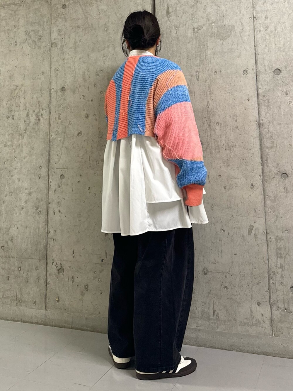 オレンジ系のニット/セーター、ホワイト系のワンピース、ブラック系のデニムパンツを着用したレディースの冬コーディネートの2枚目の写真