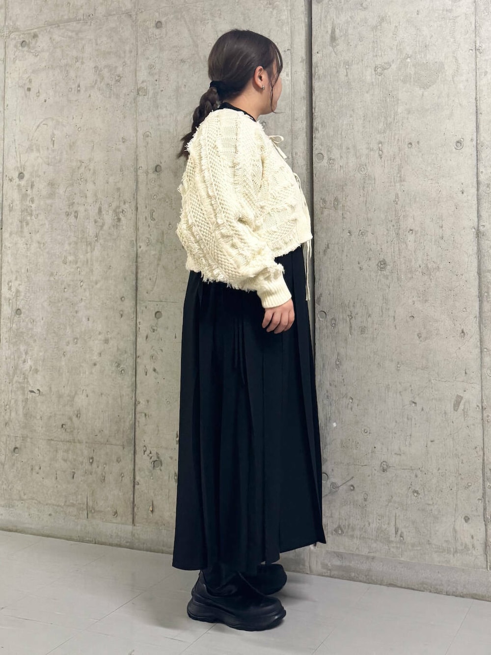 ブラック系のブーツ、ホワイト系のカーディガン/ボレロ、ブラック系のワンピースを着用したレディースの冬コーディネートの2枚目の写真