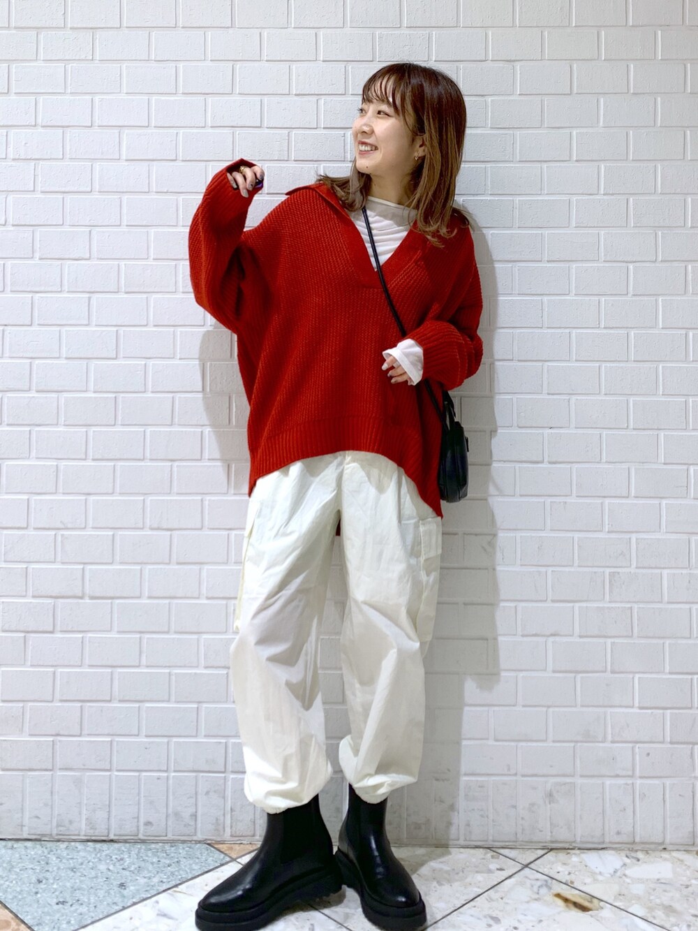 オレンジ系のトップス、ホワイト系のパンツ、ブラック系のバッグを着用したレディースの秋コーディネートの2枚目の写真