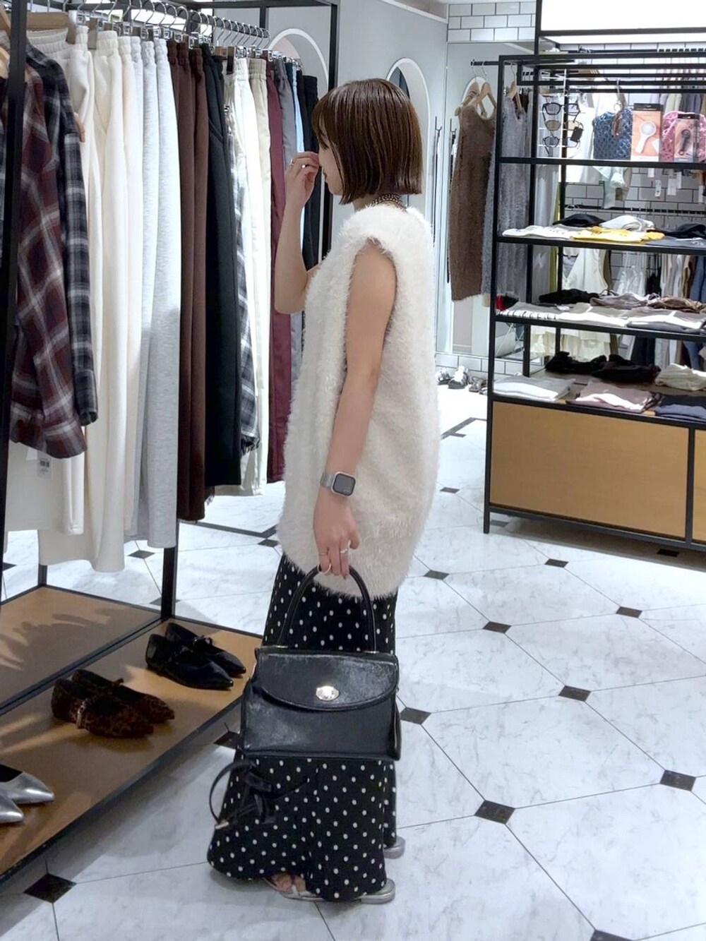 シルバー系のサンダル、ブラック系のスカート、ホワイト系のベストを着用したレディースの夏コーディネートの2枚目の写真