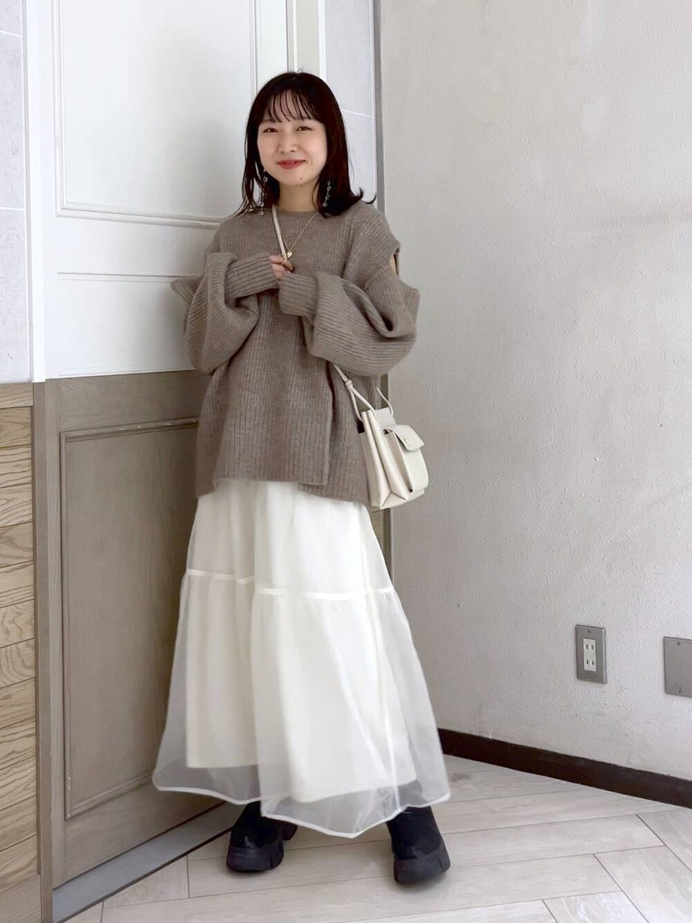 ホワイト系のショルダーバッグ、ブラック系のブーツ、ホワイト系のスカートを着用したレディースの秋コーディネートの2枚目の写真