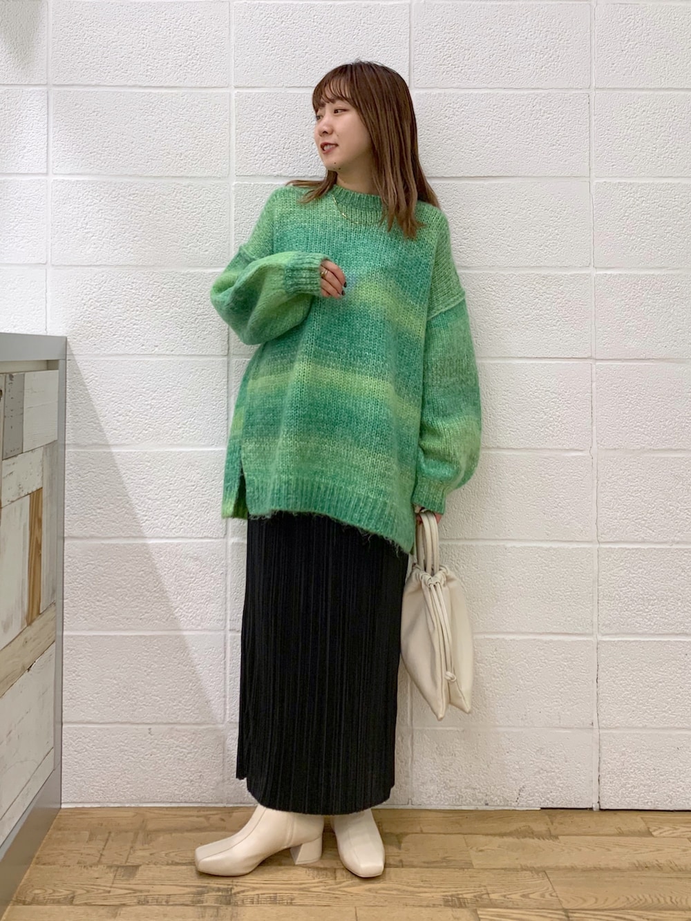 グリーン系のトップス、ブラック系のスカート、ホワイト系のショルダーバッグを着用したレディースの秋コーディネートの2枚目の写真