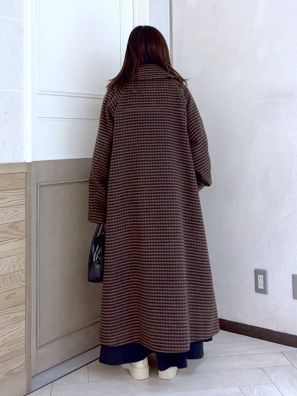 ブラウン系のノーカラーコート、ホワイト系のブーツ、ブラック系のワンピースを着用したレディースの冬コーディネートの4枚目の写真