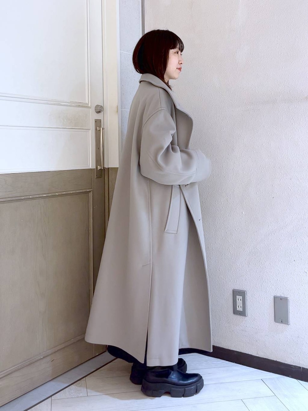 ブラック系のスカート、ホワイト系のチェスターコート、ブラック系のブーツを着用したレディースの冬コーディネートの3枚目の写真