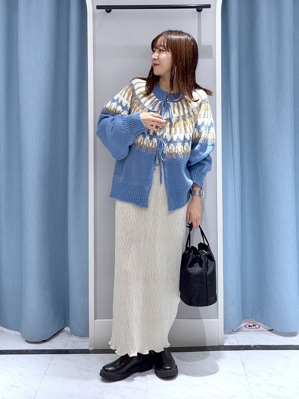 ブラック系のブーツ、ホワイト系のスカート、ブラック系のハンドバッグを着用したレディースの冬コーディネートの2枚目の写真