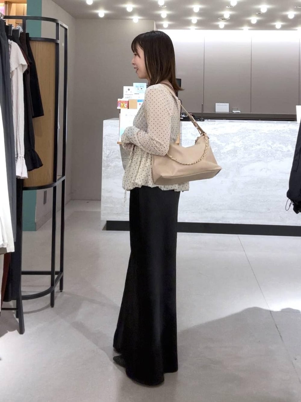 ブラック系のスカート、ベージュ系のショルダーバッグ、ブラック系のパンプスを着用したレディースの春コーディネートの2枚目の写真