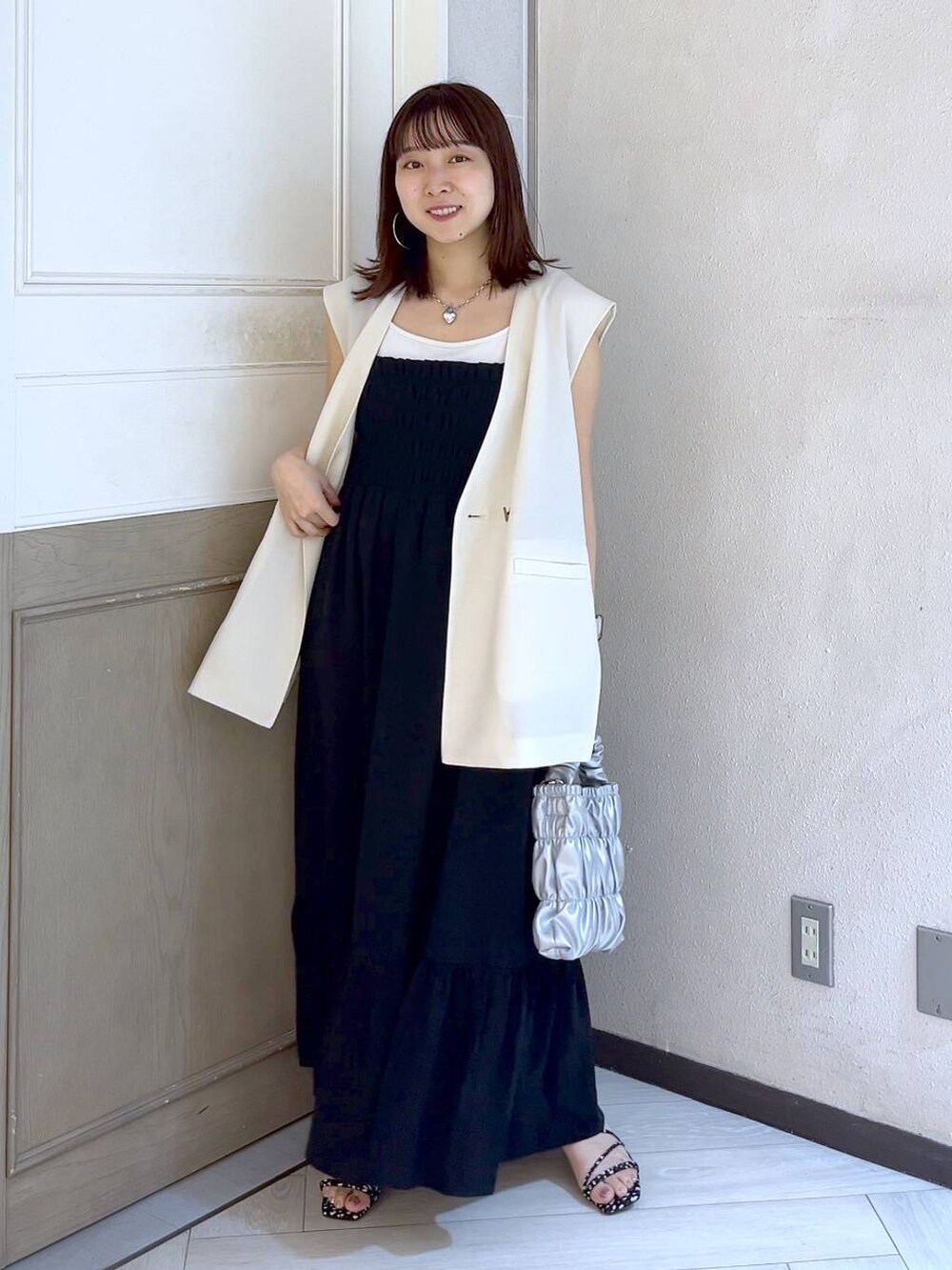 グレー系のショルダーバッグ、ブラック系のワンピース、ブラック系のサンダルを着用したレディースの夏コーディネートの2枚目の写真