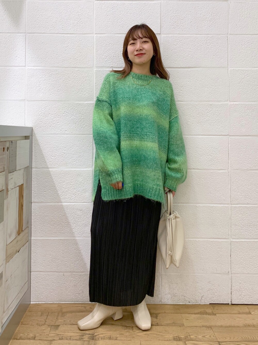 グリーン系のトップス、ブラック系のスカート、ホワイト系のショルダーバッグを着用したレディースの秋コーディネートの3枚目の写真