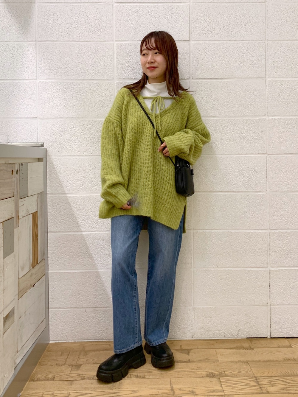 グリーン系のトップス、ブルー系のデニムパンツ、ブラック系のバッグを着用したレディースの秋コーディネートの2枚目の写真