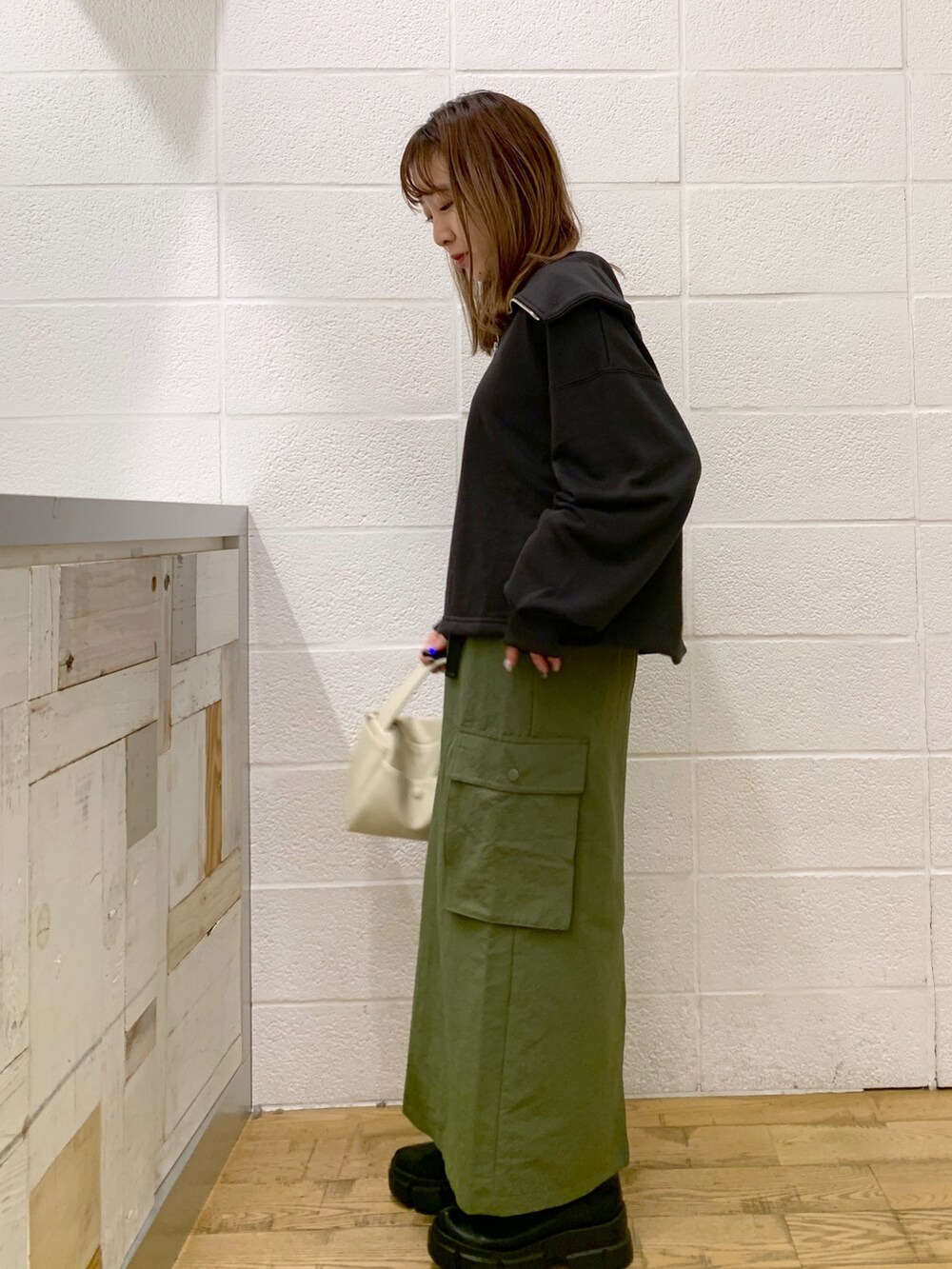 グレー系のトップス、グリーン系のスカート、ホワイト系のバッグを着用したレディースの秋コーディネートの3枚目の写真