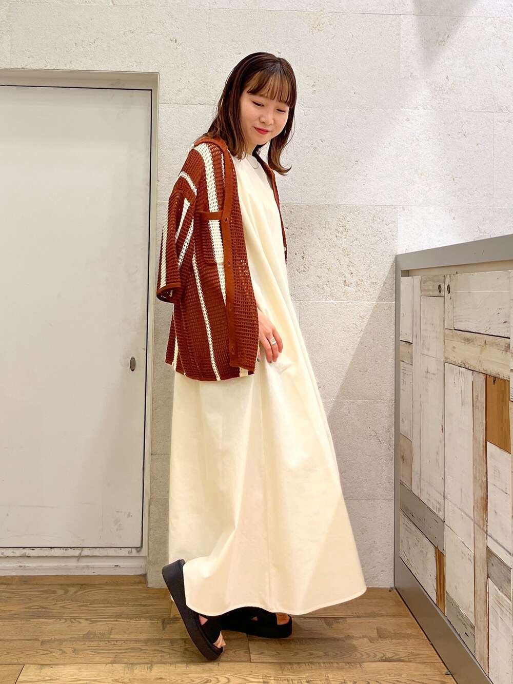 ホワイト系のワンピース、ブラウン系のトップス、ブラック系のシューズを着用したレディースの春コーディネートの2枚目の写真