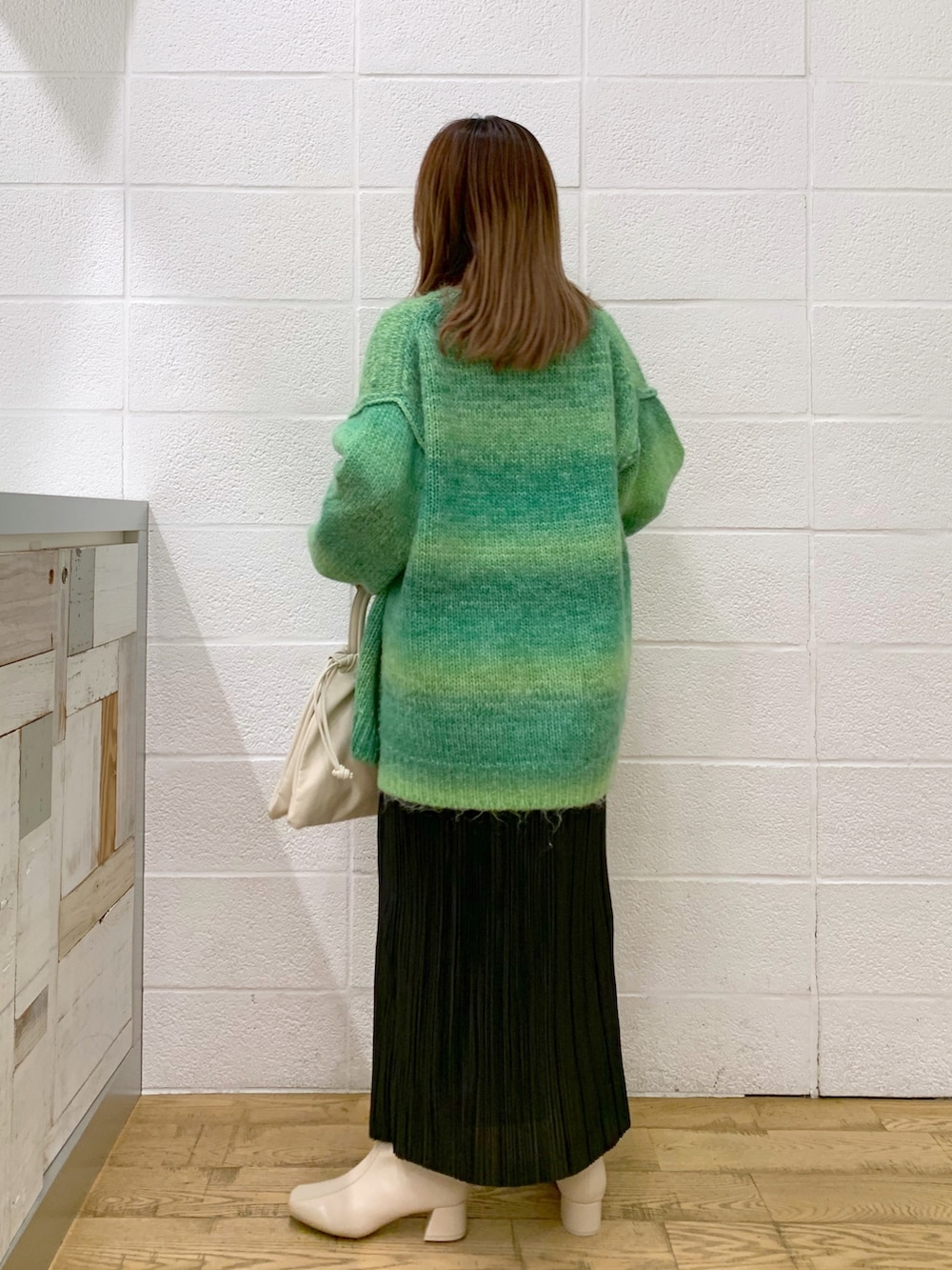 グリーン系のトップス、ブラック系のスカート、ホワイト系のショルダーバッグを着用したレディースの秋コーディネートの5枚目の写真