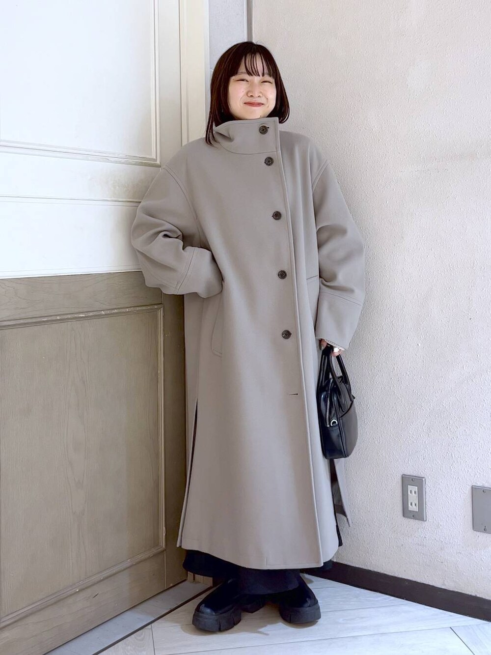 ブラック系のスカート、ホワイト系のチェスターコート、ブラック系のブーツを着用したレディースの冬コーディネートの2枚目の写真