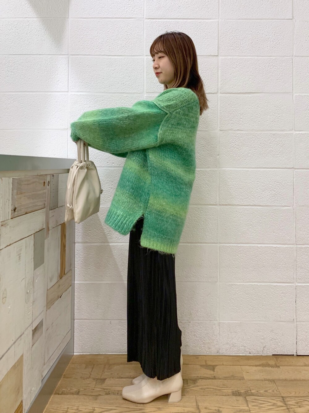 グリーン系のトップス、ブラック系のスカート、ホワイト系のショルダーバッグを着用したレディースの秋コーディネートの4枚目の写真