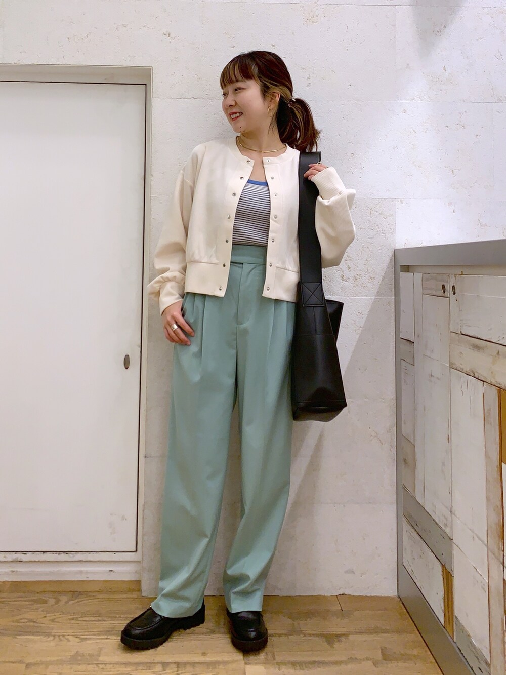 ホワイト系のトップス、グリーン系のパンツ、ブラック系のバッグを着用したレディースの春コーディネートの2枚目の写真