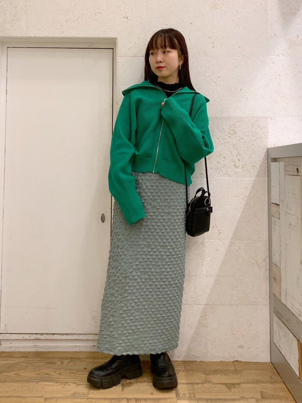 グリーン系のトップス、グリーン系のスカート、ブラック系のショルダーバッグを着用したレディースの冬コーディネートの2枚目の写真