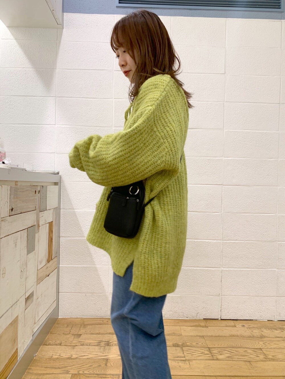 グリーン系のトップス、ブルー系のデニムパンツ、ブラック系のバッグを着用したレディースの秋コーディネートの4枚目の写真