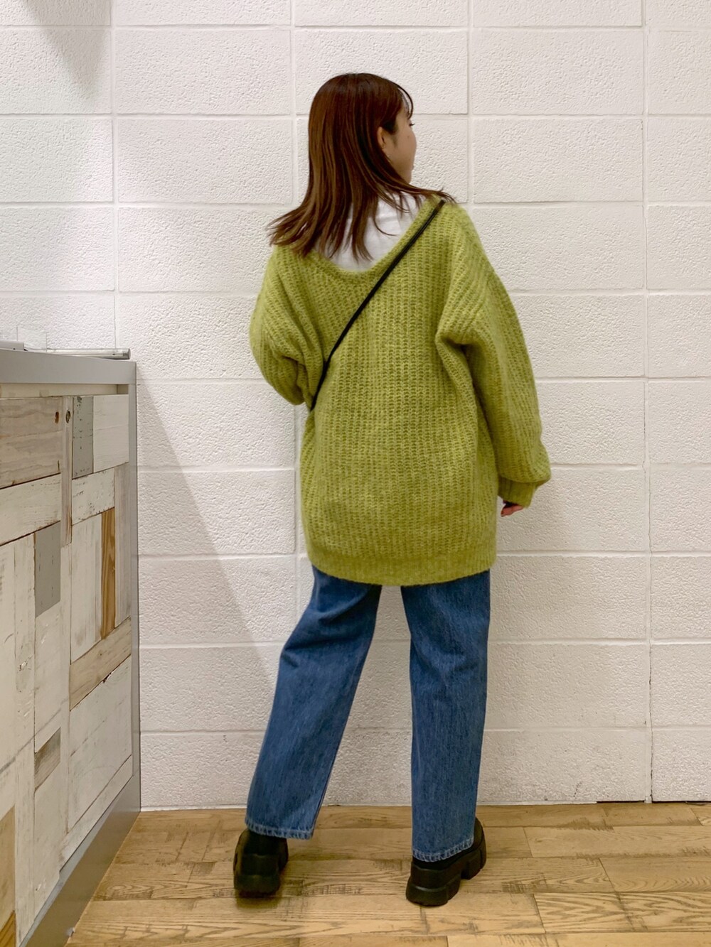 グリーン系のトップス、ブルー系のデニムパンツ、ブラック系のバッグを着用したレディースの秋コーディネートの3枚目の写真