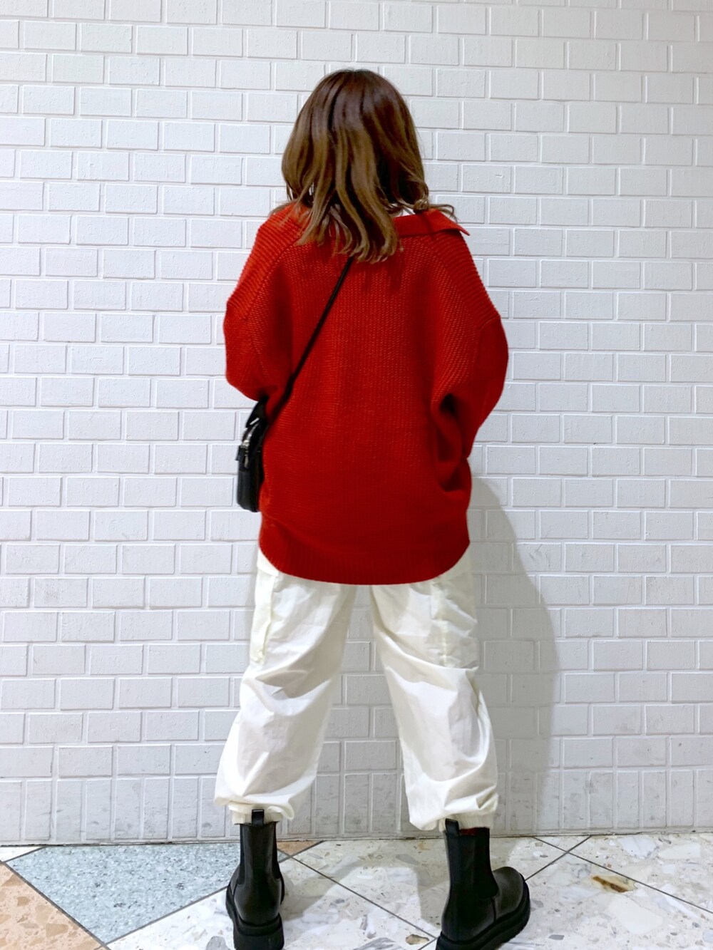 オレンジ系のトップス、ホワイト系のパンツ、ブラック系のバッグを着用したレディースの秋コーディネートの5枚目の写真