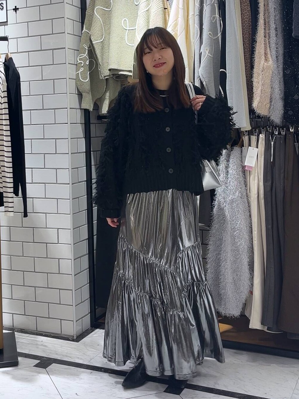 シルバー系のショルダーバッグ、ブラック系のブーツ、グレー系のスカートを着用したレディースの冬コーディネートの2枚目の写真