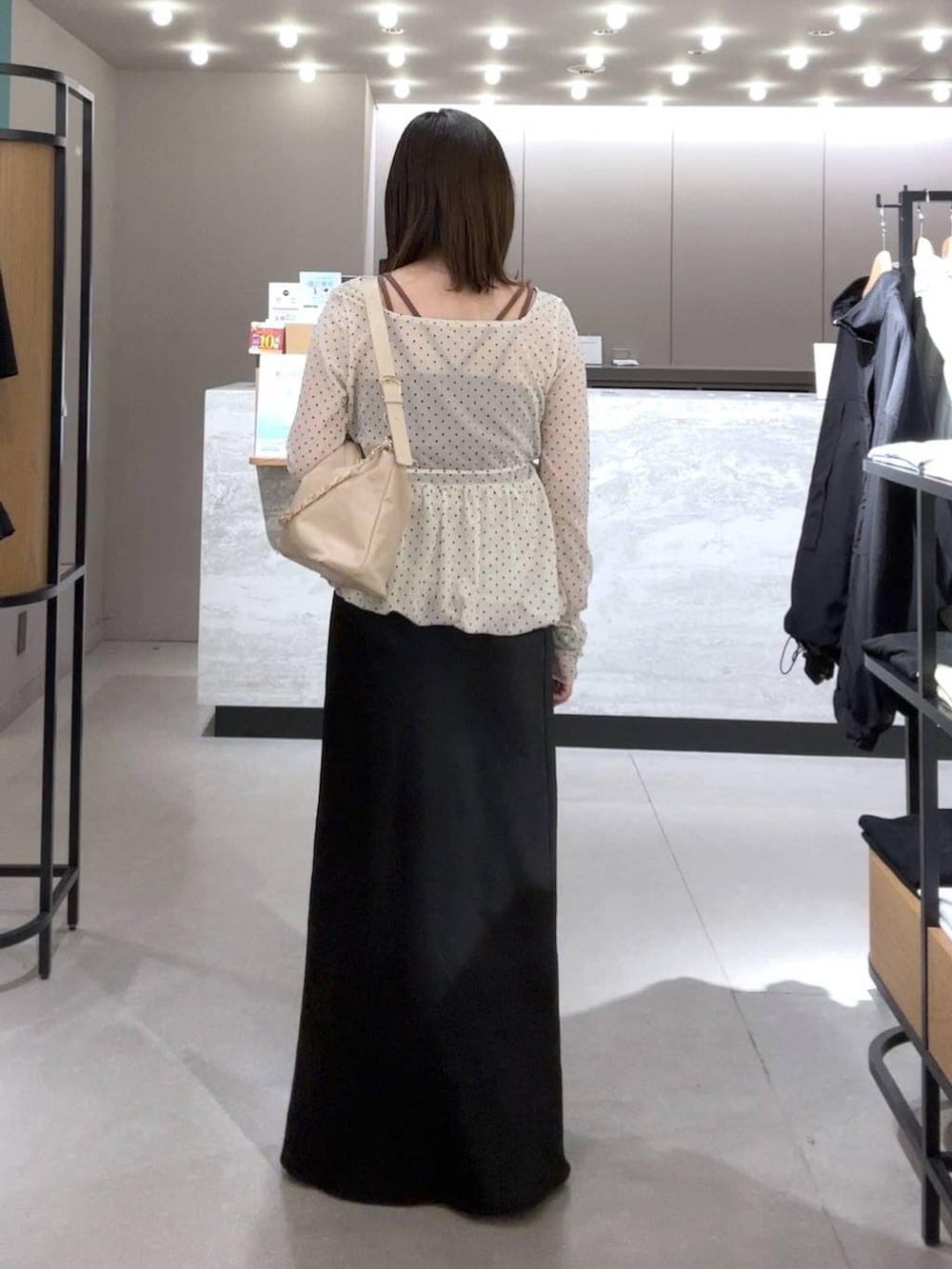 ブラック系のスカート、ベージュ系のショルダーバッグ、ブラック系のパンプスを着用したレディースの春コーディネートの3枚目の写真