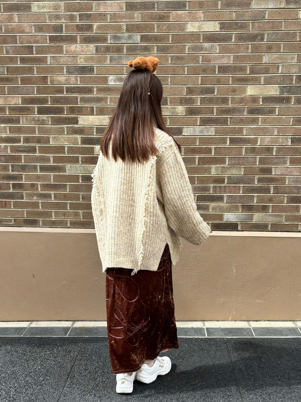 ブラウン系のスカート、ホワイト系のニット/セーター、ホワイト系のスニーカーを着用したレディースの冬コーディネートの2枚目の写真
