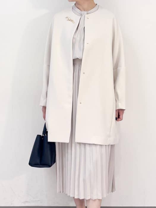 ホワイト系のノーカラーコート、ベージュ系のワンピース、ブラック系のハンドバッグを着用したレディースの冬コーディネートの3枚目の写真