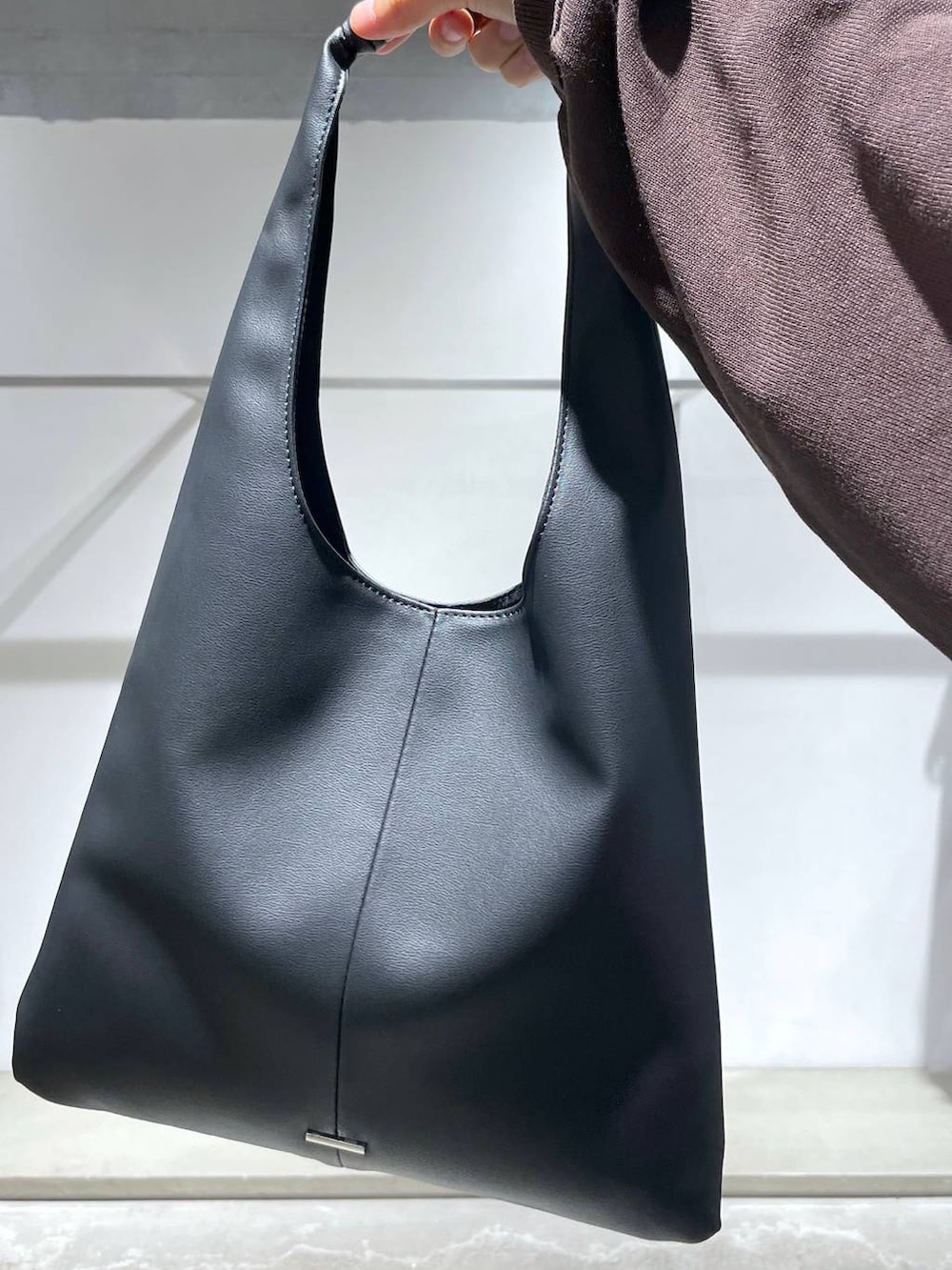 ブラウン系のニット/セーター、ブラック系のトートバッグ、ブラック系のスラックスを着用したメンズの夏コーディネートの6枚目の写真