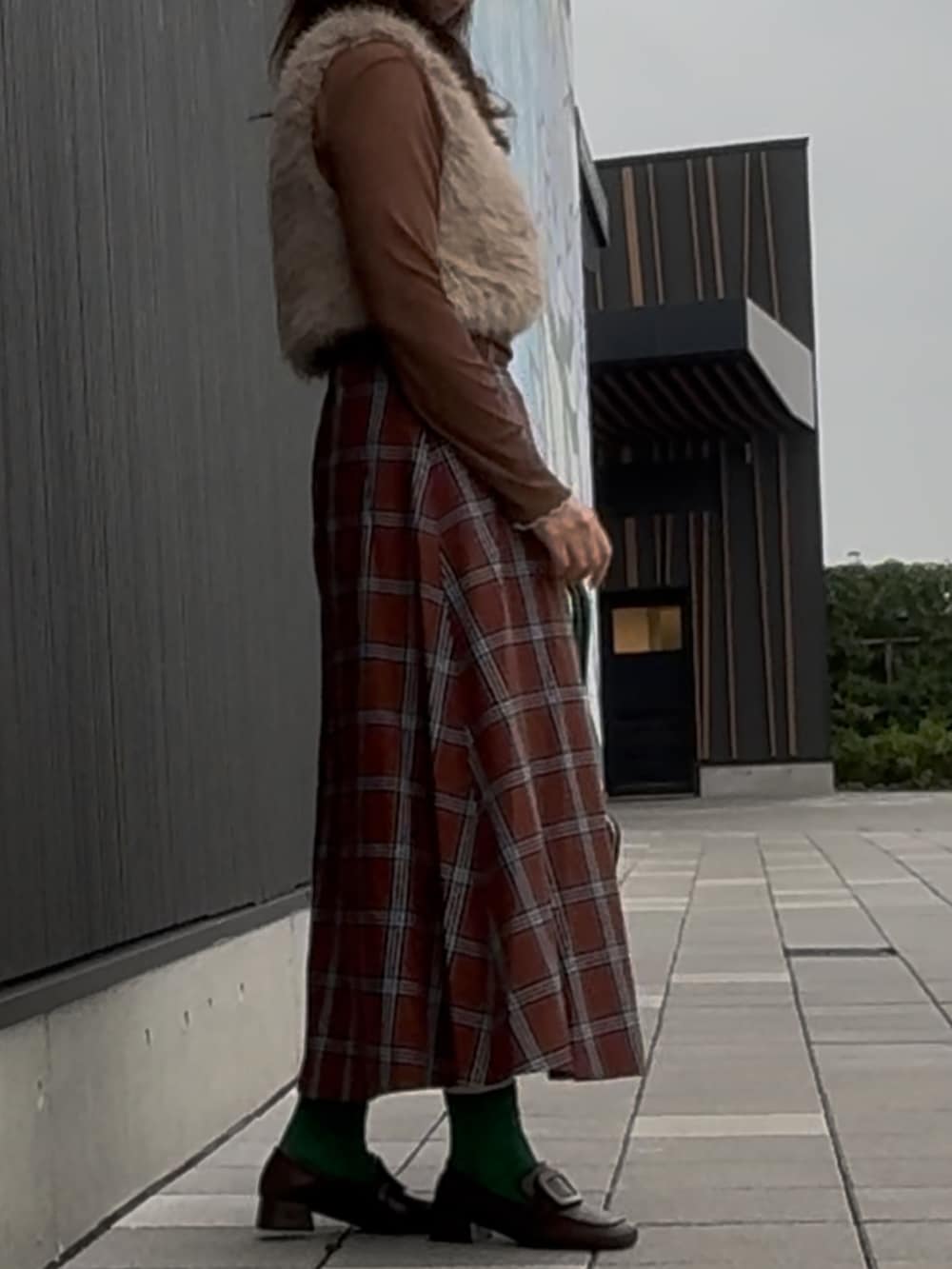 グリーン系のショルダーバッグ、ブラウン系のスカート、ベージュ系のベストを着用したレディースの秋コーディネートの2枚目の写真