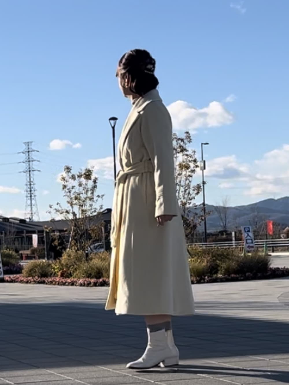 イエロー系のチェスターコート、ホワイト系のショルダーバッグ、ホワイト系のスカートを着用したレディースの冬コーディネートの3枚目の写真