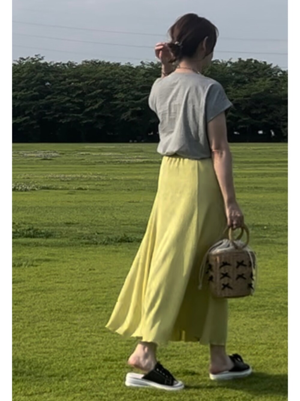 グレー系のTシャツ/カットソー、イエロー系のスカート、ブラック系のサンダルを着用したレディースの夏コーディネートの2枚目の写真