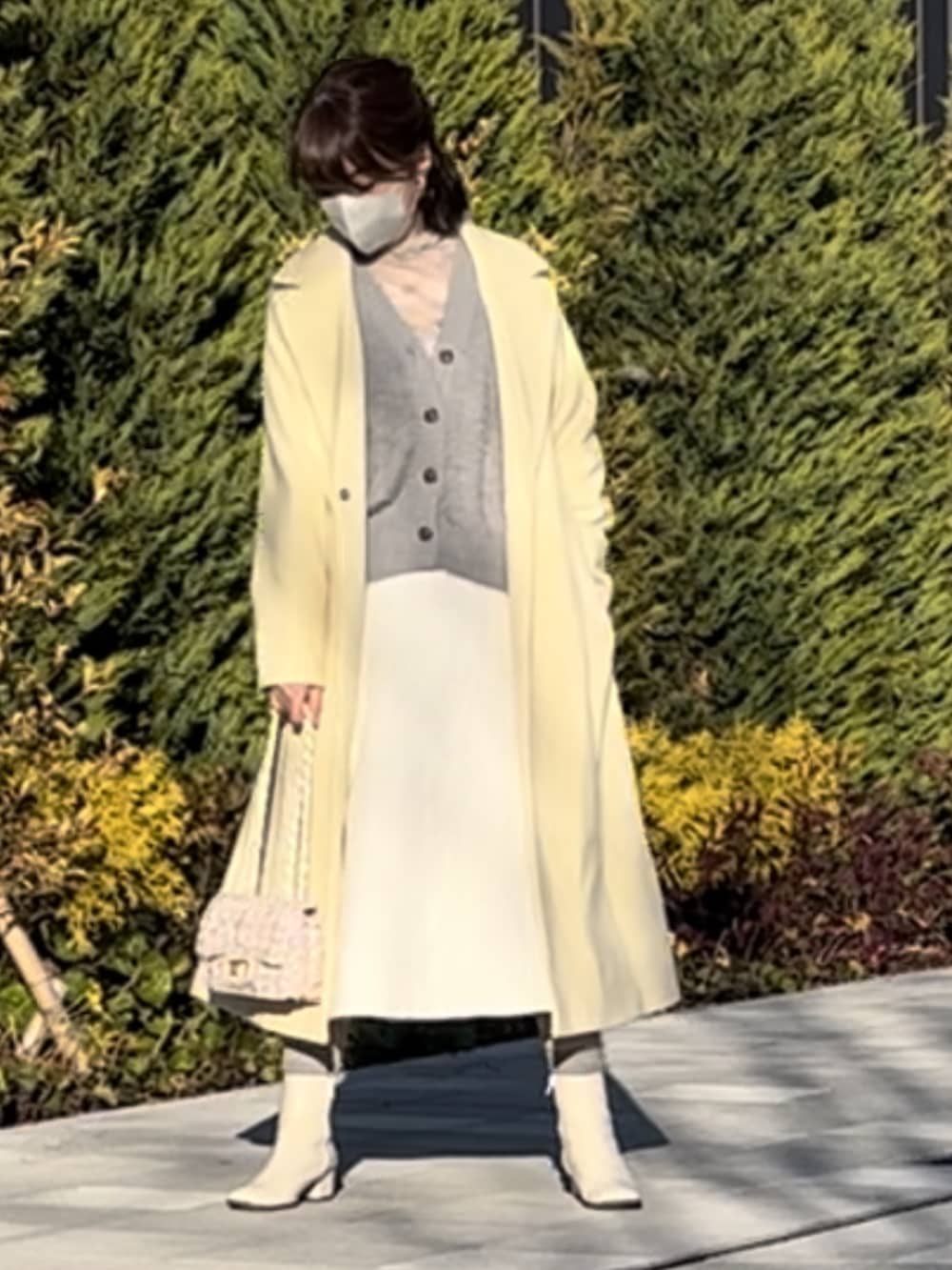 イエロー系のチェスターコート、ホワイト系のショルダーバッグ、ホワイト系のスカートを着用したレディースの冬コーディネートの2枚目の写真