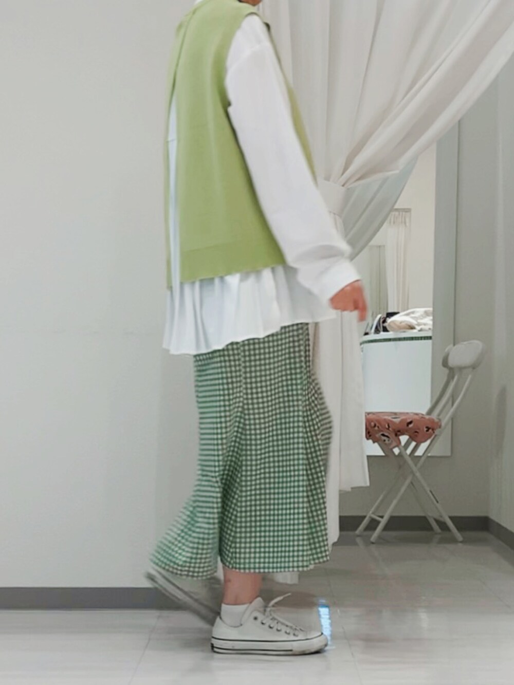 グリーン系のベスト、グリーン系のスカート、ホワイト系のスニーカーを着用したレディースの春コーディネートの2枚目の写真