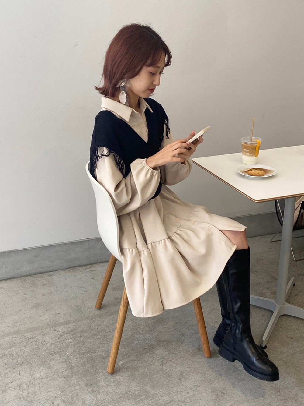 ベージュ系のシャツワンピース、ホワイト系のショルダーバッグ、ブラック系のブーツを着用したレディースの春コーディネートの2枚目の写真