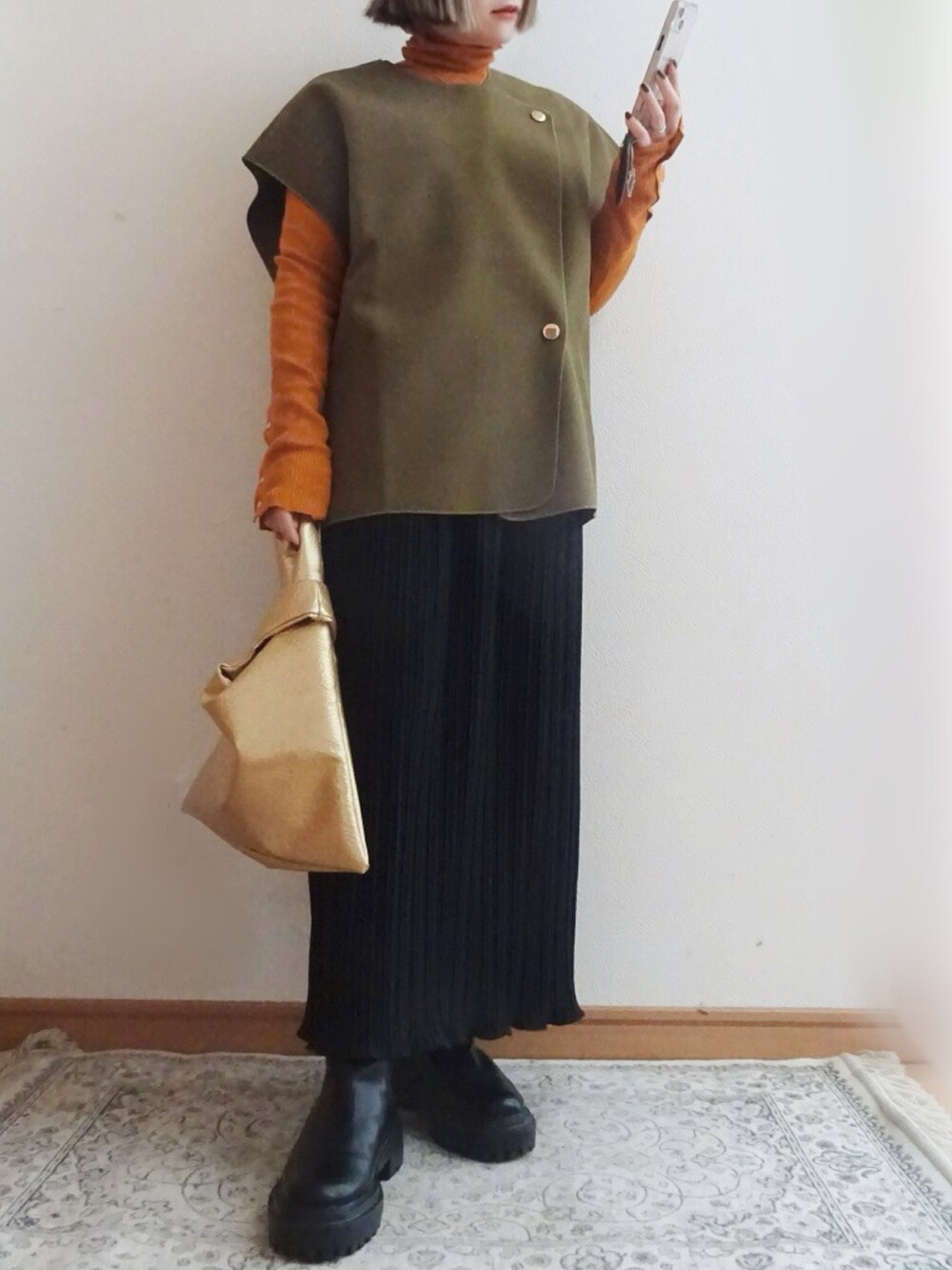 グリーン系のベスト、ブラック系のスカート、ゴールド系のバッグを着用したレディースの冬コーディネートの2枚目の写真